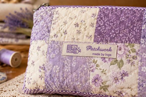 Luonnonvärinen puuvillaetiketti violetilla tekstillä patchwork-laukussa