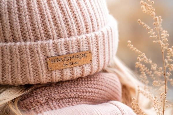 Suorakaiteinen vaaleanruskea keinonahkamerkki "Handmade by Bine" vaaleanpunaisessa pipossa.